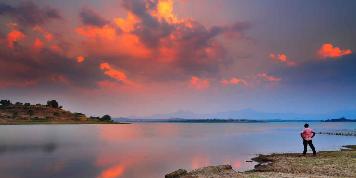 Man standing observing the sunset over a serene lake.