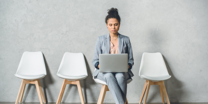 Middle-aged woman sitting typing, there are 2 empty chairs to her left and one to the right.