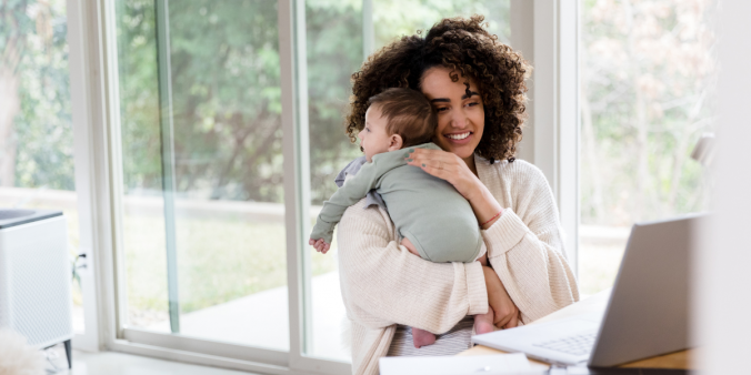 A woman sat in front of a laptop holding a baby.