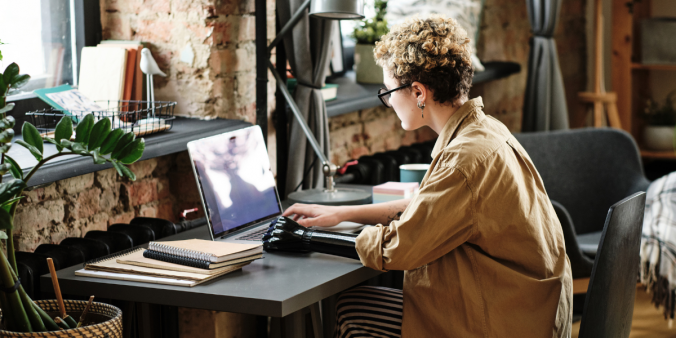 A person is sat at a desk in a dimly lit room typing on a laptop.