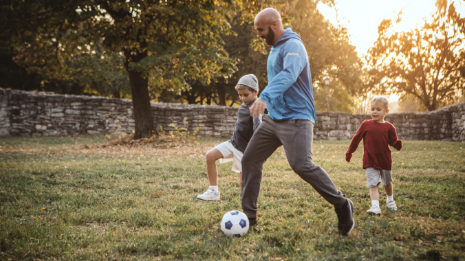 A man and two children playing soccer outside in the spring.