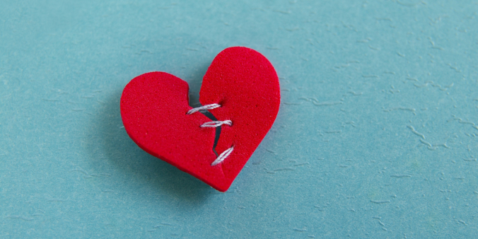 A red foam heart with stitches laying on a blue table.