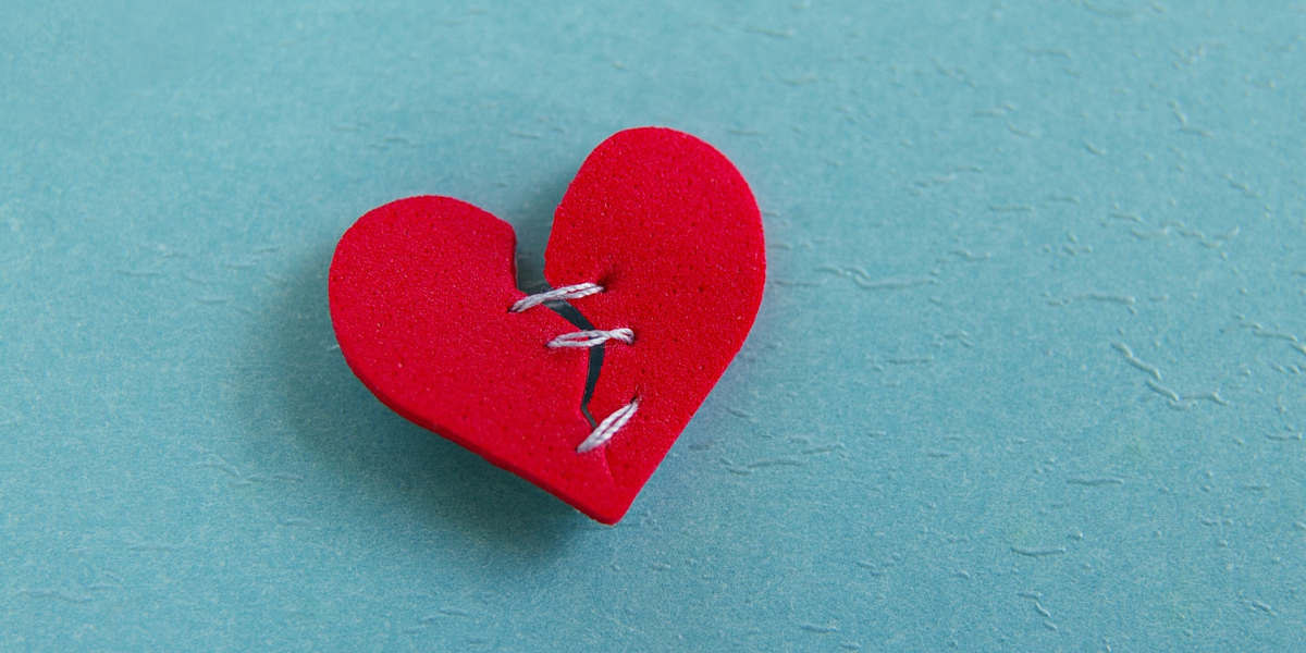 A red foam heart with stitches laying on a blue table.