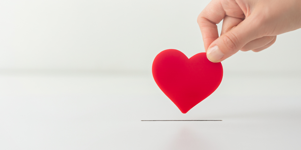 A hand is holding a red foam heart above a slot in a white box.