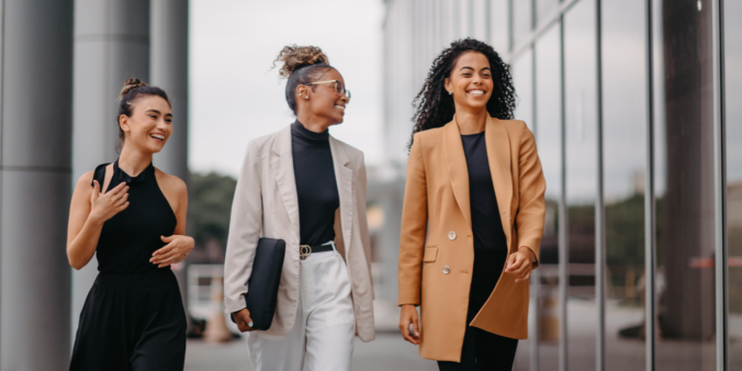 Three women are walking outside of an office building smiling and chatting.