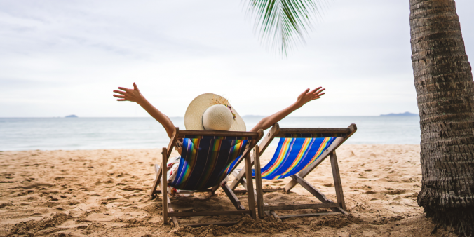 A woman laying on a beach chair in the sand with her arms in the air. The water is icy blue.