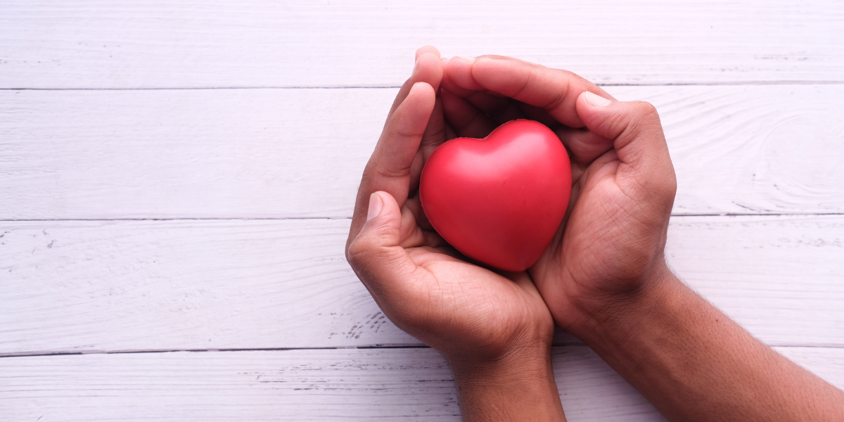 Two hands holding a red foam heart are resting on a white table.