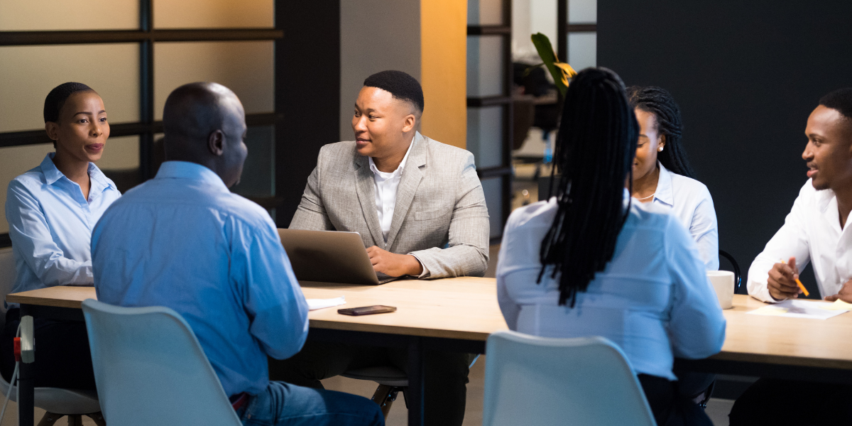 A group of individuals are sat at a board room table having a meeting.