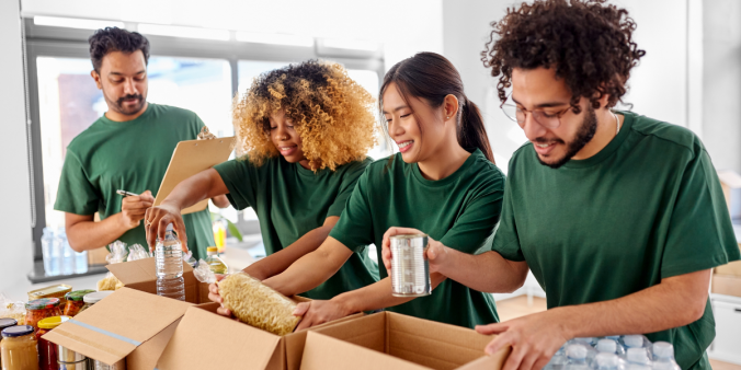 A group of four individuals wearing green shirts are packing food at a food bank.