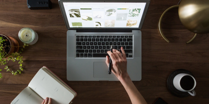 Laptop sitting open on a wooden desk with an individual typing on the keyboard.