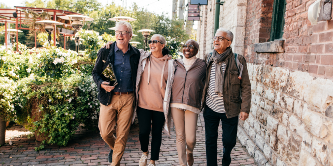 A group of older individuals walking arm in arm down a cobblestone street midday.