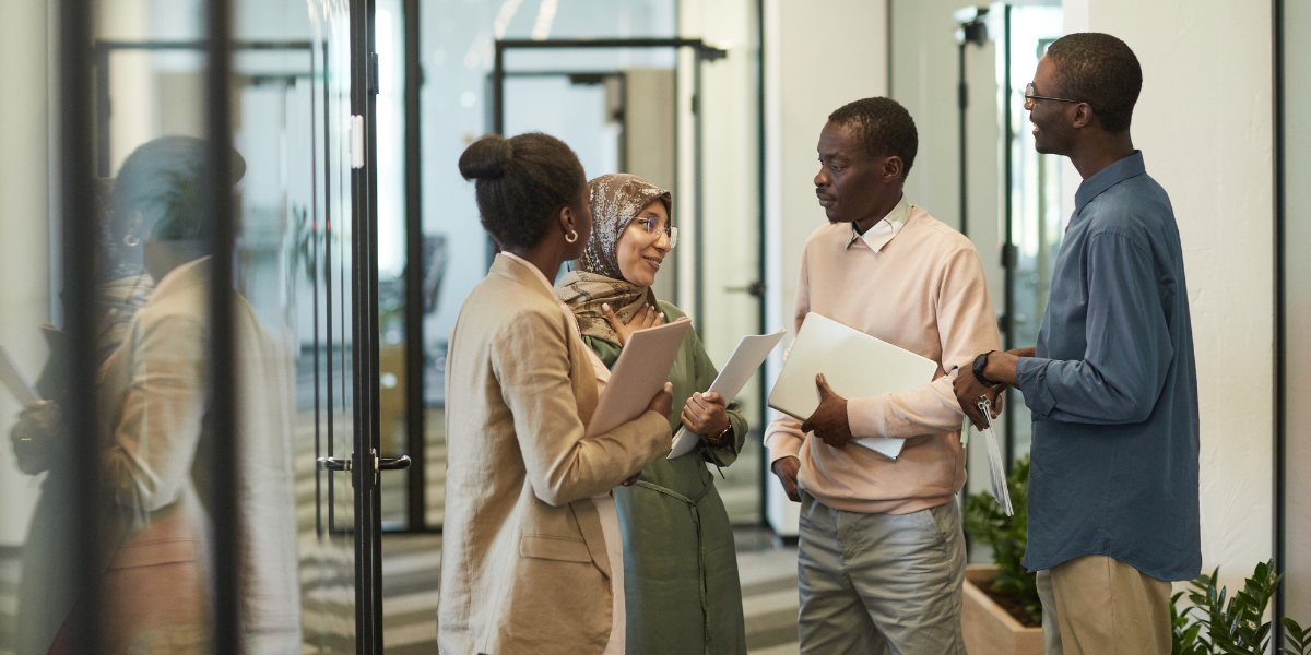 Four people standing in a hallway conversing holding paperwork.