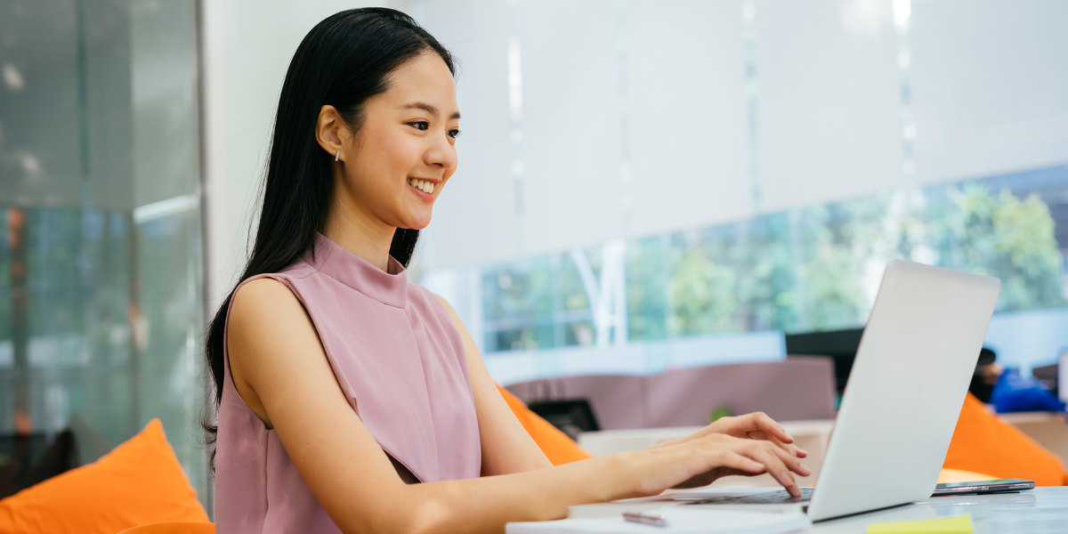 A woman sitting at a desk typing on her computer smiling and working.